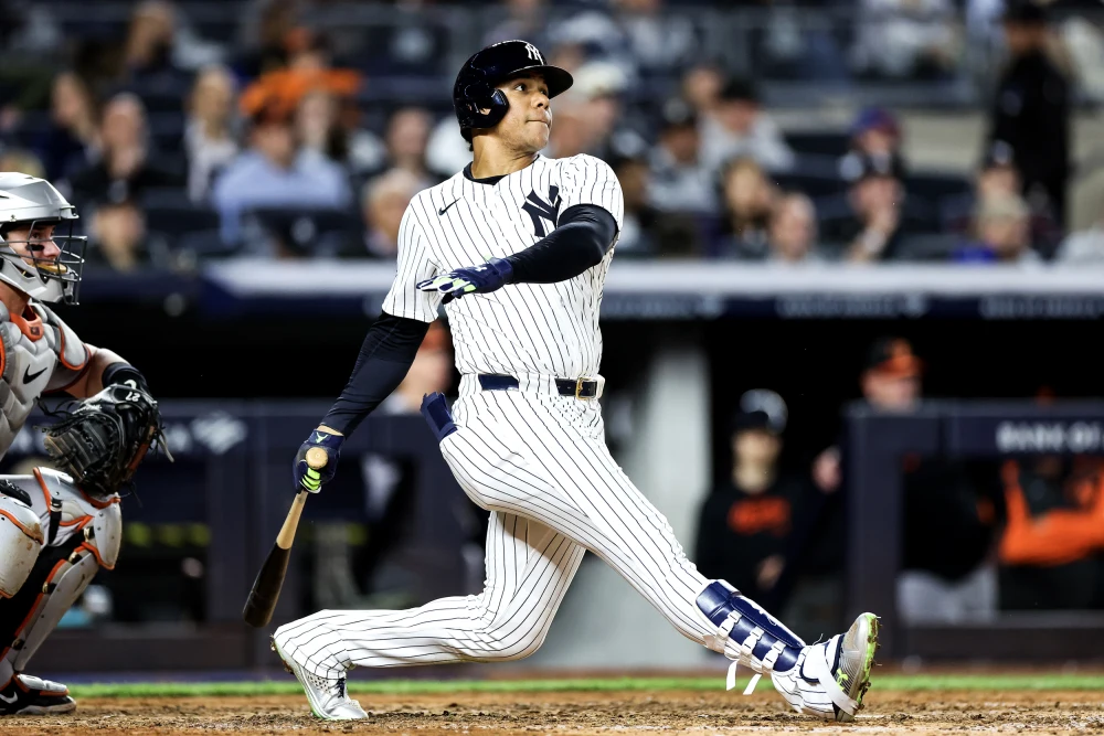 New York Yankees batter in pinstripes swings at a pitch during a baseball game, with catcher and crowd in the background.